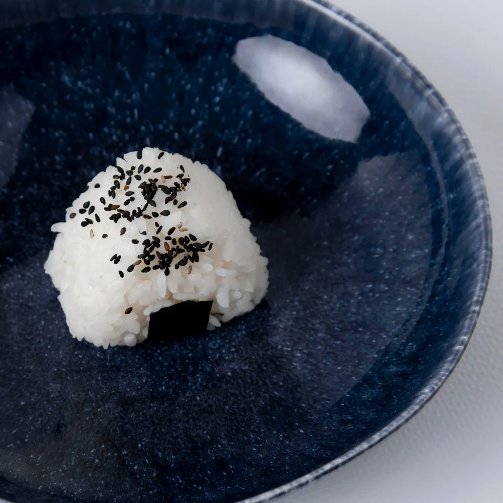 Onigiri japonais garni de graines de sésame noir, posé sur une assiette en céramique bleue nuit