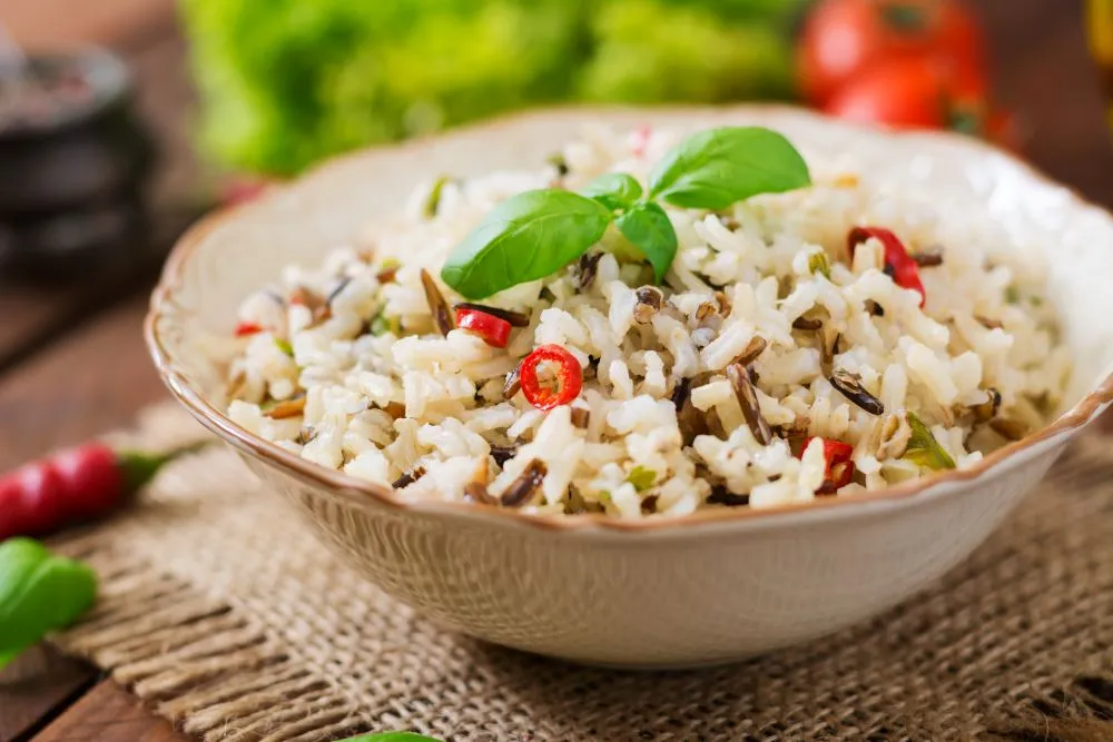 Bol individuel remplit de riz noir et blanc avec des rondelles de mini piment et une feuille de basilic sur le dessus.